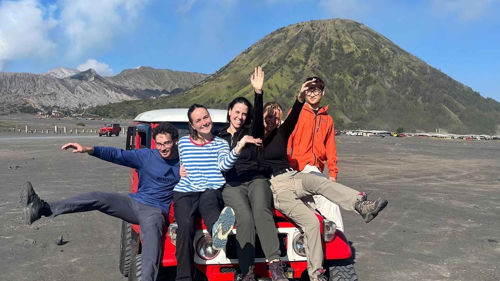 A group of people on a red vehicle with a mountainous landscape in the background. 1