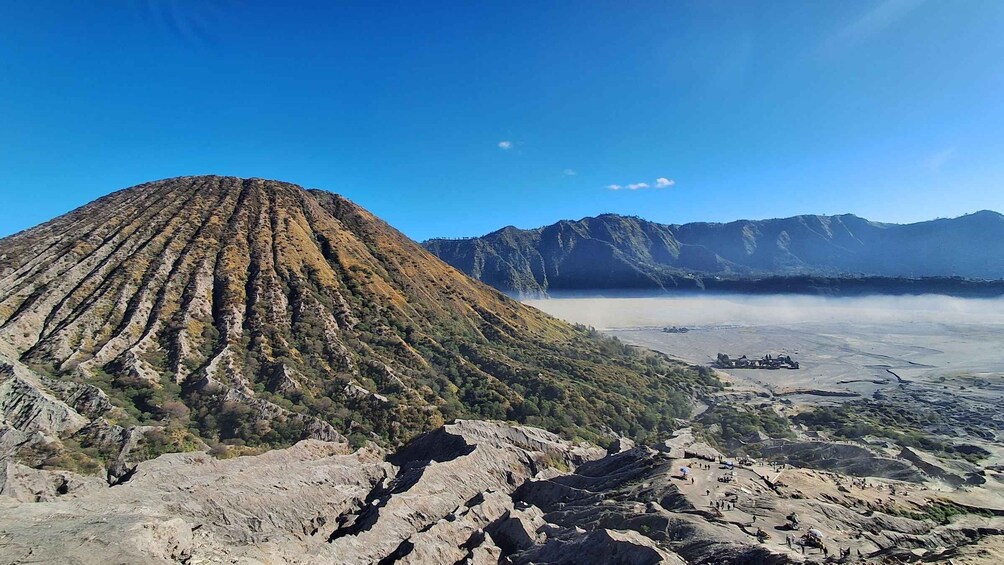 A mountain with a distinct ridge pattern, a valley with a misty lake, and distant mountains under a clear sky. 5