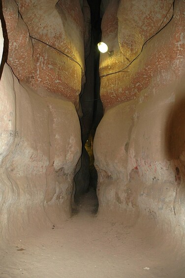 A narrow, rocky cave passage with a single light source at the end. 5