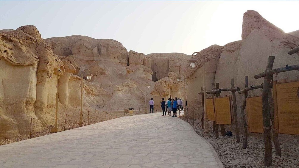 A pathway leading through a rocky canyon with visitors and informational signs. 1