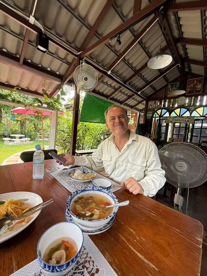 A person dining at an outdoor restaurant with a table set for a meal, including bowls of soup and rice, and a water bottle on the table. 5