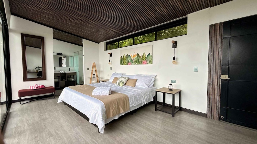 A modern bedroom with a bed, a bench, a ladder, a small table, and a door. 3