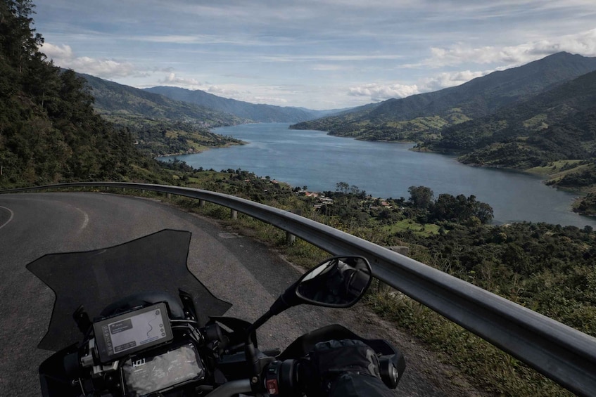 A motorcycle on a winding road with a lake and mountains in the background. 1