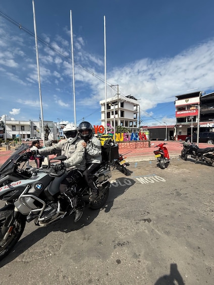 A person on a motorcycle with a helmet, a building with a sign that reads 'BOMBEROS,' and a clear blue sky. 2