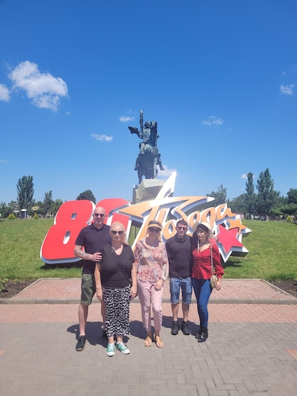 A group of people standing in front of a large outdoor sign with a statue in the background. 4