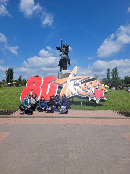 A group of people posing in front of a large outdoor sign with a statue in the background. 5