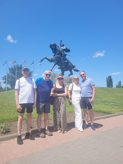 A group of people standing in front of a statue on a sunny day. 3