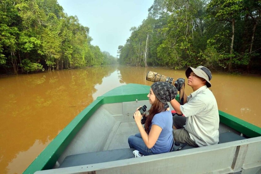 A boat with two people, one holding binoculars, on a river surrounded by dense green forest. 1