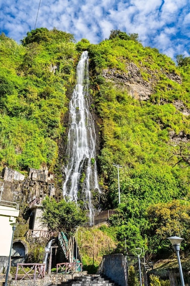 A waterfall cascading down a lush green hillside, with a stone bridge and steps leading up to it. 2