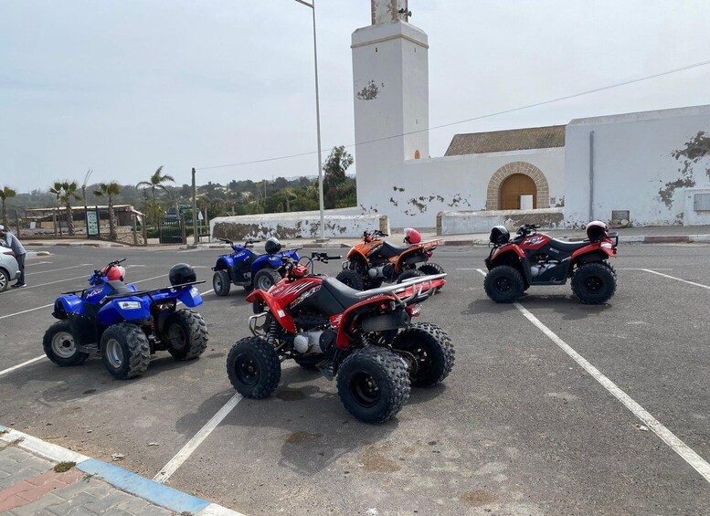 A parking lot with several quad bikes, a white building with a tower, and palm trees in the background. 2