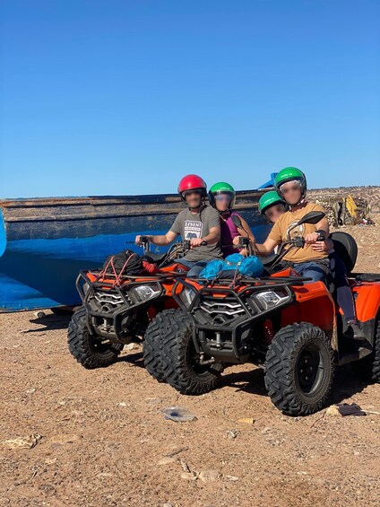 Three people on an ATV in a dry, rocky area with a blue body of water in the background. 4
