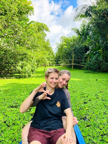 Two people sitting on a grassy area surrounded by lush greenery and trees. 2