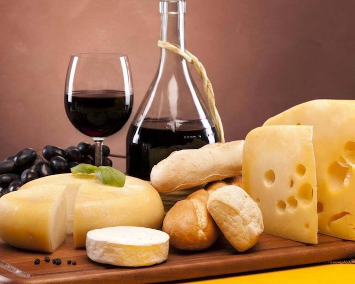 A variety of cheeses, bread, and a bottle of wine on a wooden board. 1