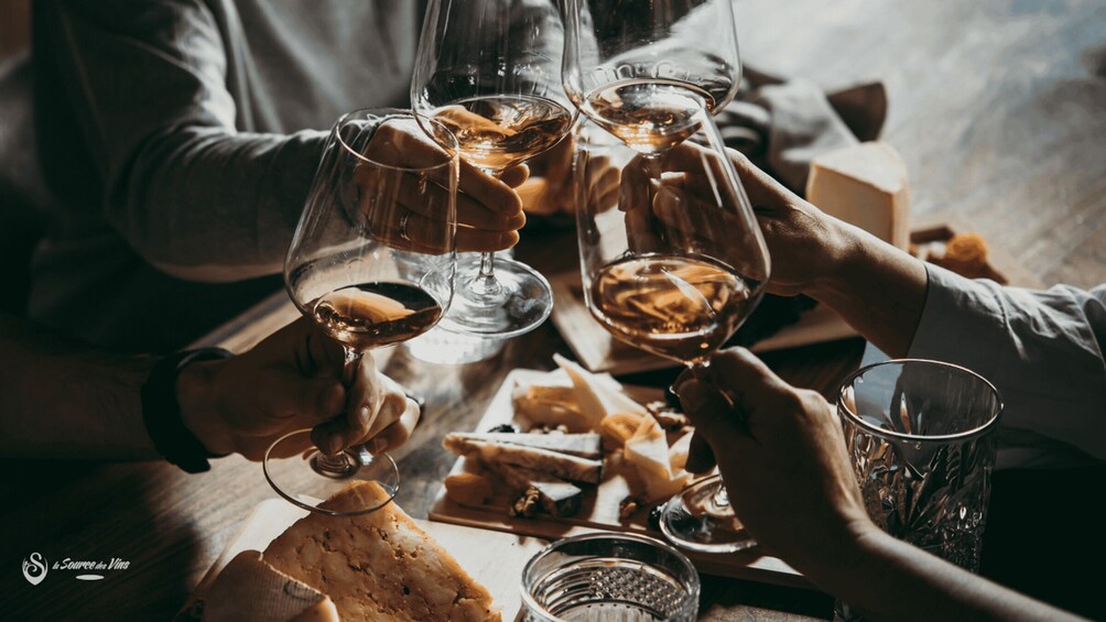 People toasting with wine glasses, cheese, and bread on a wooden table. 2