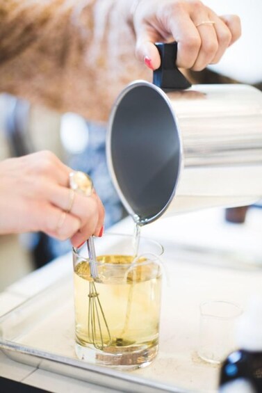 A person pouring a liquid from a container into a glass with a whisk inside. 3