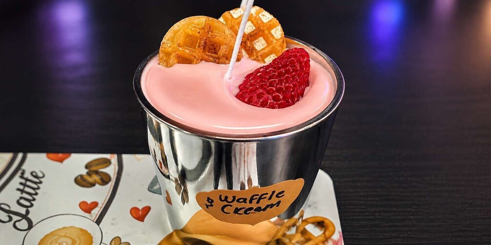 A waffle cream drink in a metal cup with a waffle and a strawberry on top. 5