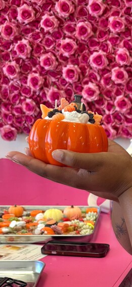 A hand holding a carved pumpkin with a white top, surrounded by a pink background with roses. 2