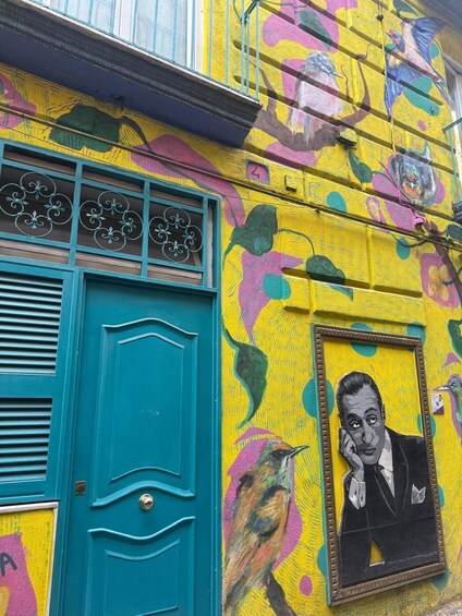 A building with a vibrant yellow facade, teal doors, and a framed portrait. 5