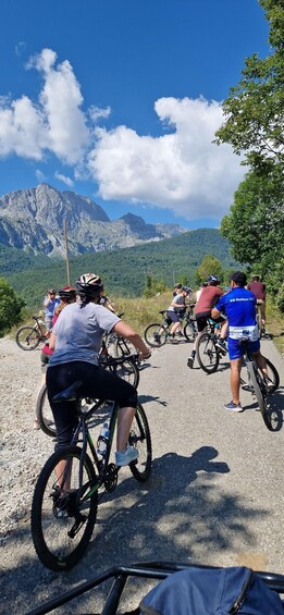 A group of cyclists on a paved path with mountains in the background. 4