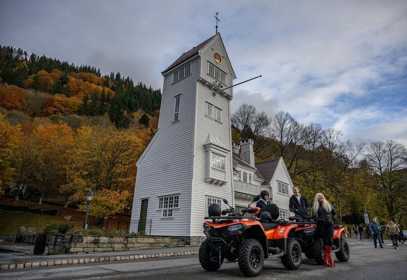 A white church with a bell tower, surrounded by autumn foliage and people on ATVs. 1