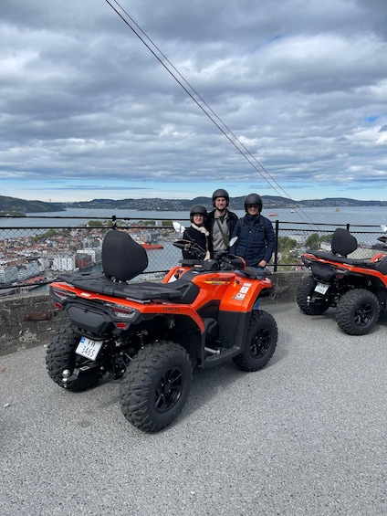 Three orange ATVs parked on a paved area with a scenic view of a bridge and water in the background. 4