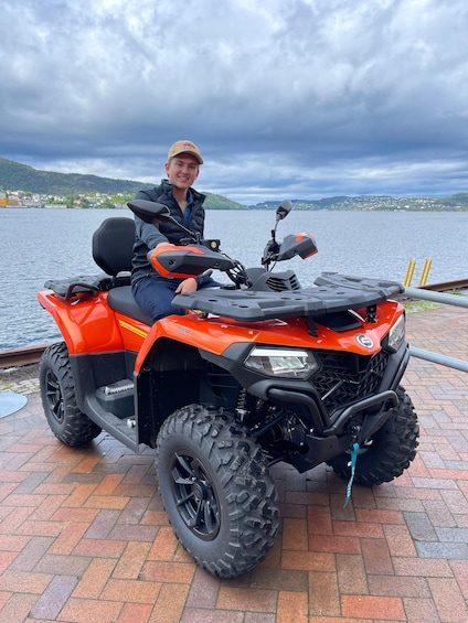 A person sitting on an orange ATV with a lake and mountains in the background. 2