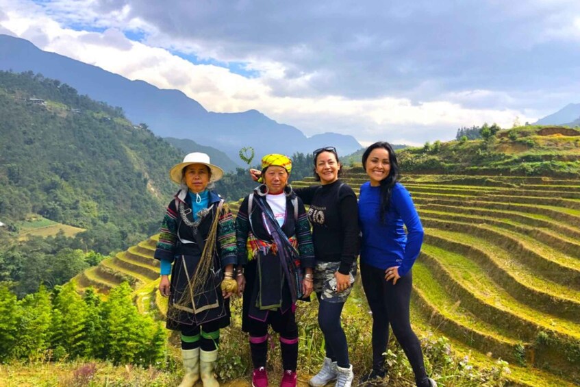 Four people standing in a terraced rice field with mountains in the background. 5