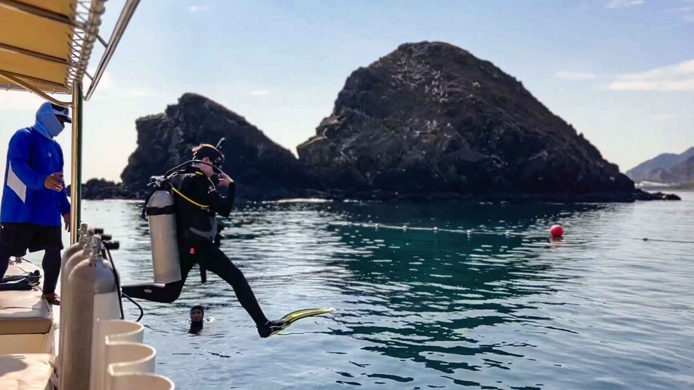 A diver in a black wetsuit with fins and a scuba tank on a boat, preparing to enter the water. 3