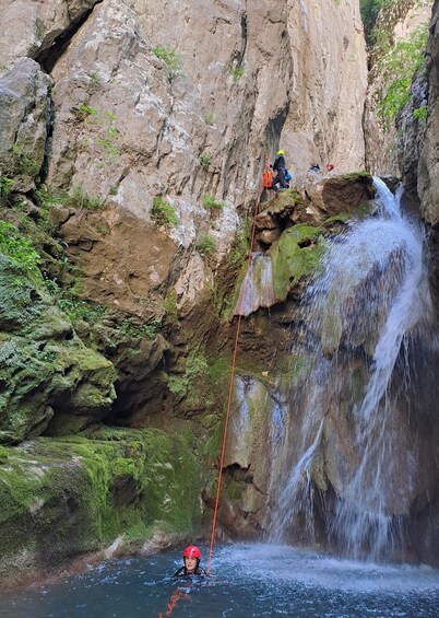 A person rappelling down a rocky cliff with a waterfall in the background. 2