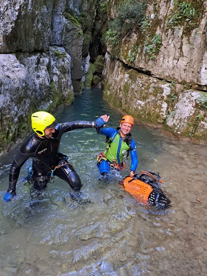 Two individuals in wetsuits and helmets near a rocky water channel. 3