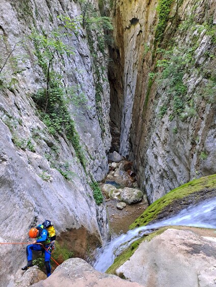 A person rappelling down a rocky cliff with a stream flowing below. 1
