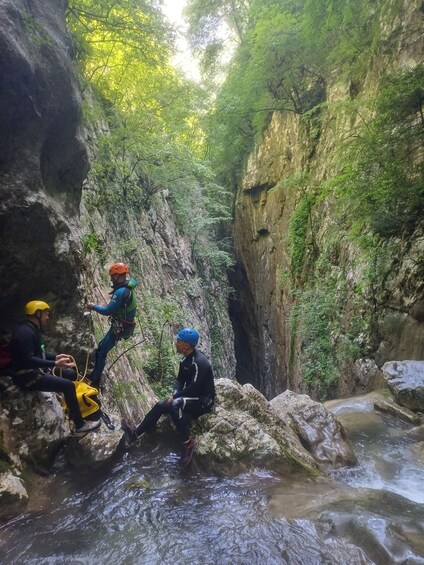 Three individuals engaged in rappelling in a rocky canyon with a stream at the bottom. 4