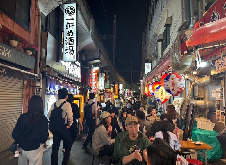 A crowded street at night with people sitting at tables, illuminated signs, and traditional lanterns. 4