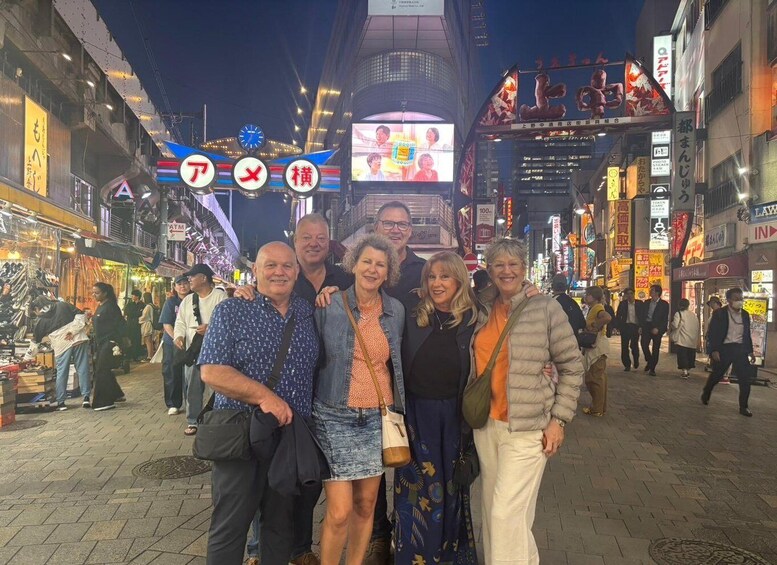 A group of people posing in a busy urban street at night with illuminated signs and storefronts. 2
