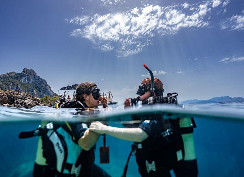 Two scuba divers underwater with a boat and rocky landscape in the background. 5