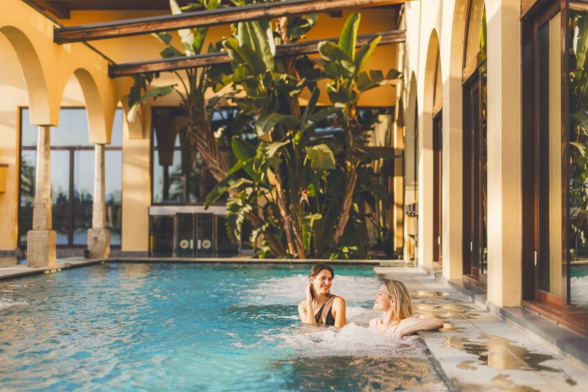 A swimming pool with two people, surrounded by a building with arches and tropical plants. 3