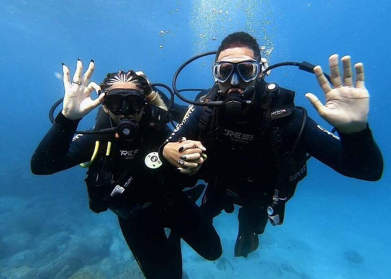 Two scuba divers underwater with their hands raised, wearing black wetsuits and scuba gear. 4