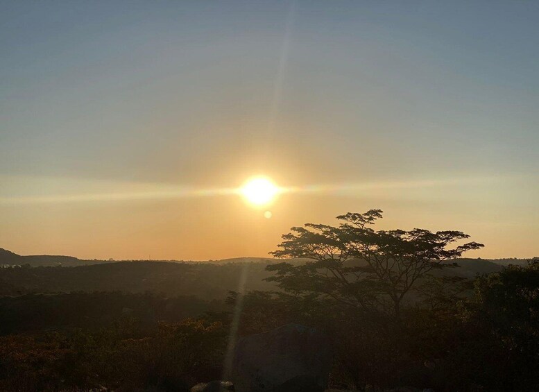 A sunset with the sun low on the horizon, casting a glow over a hilly landscape with sparse vegetation. 4