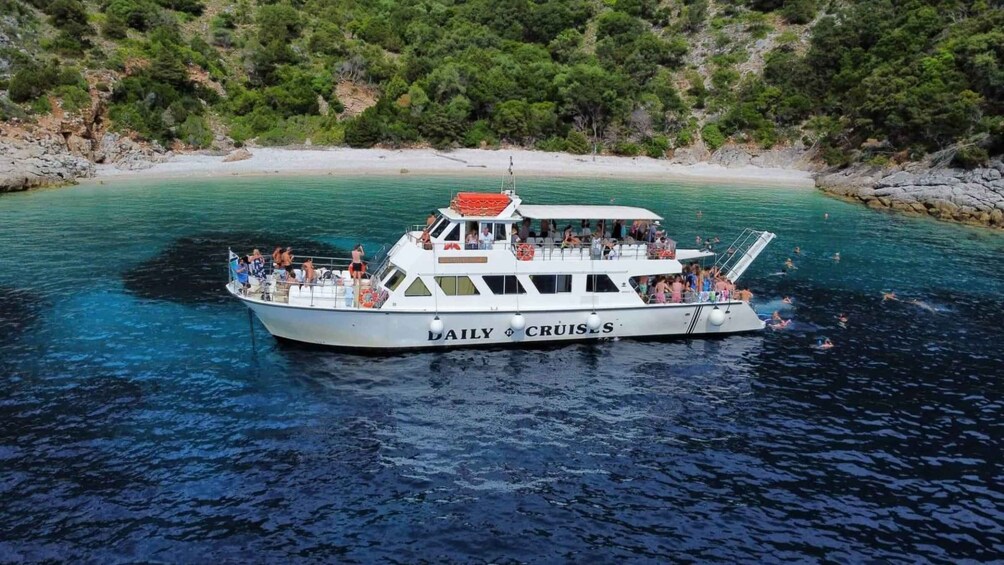 A boat named 'DAILY CRUISES' with passengers on board, surrounded by clear turquoise water and a rocky shoreline with greenery. 2