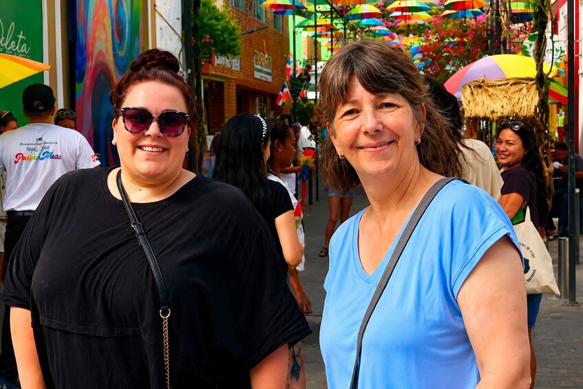Two women standing on a street with colorful umbrellas overhead. 3
