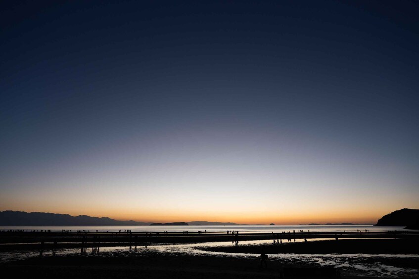 A sunset over a calm body of water with a distant mountain range and a pier with people. 2