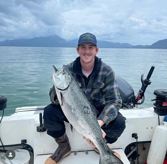A person holding a large fish on a boat with mountains in the background. 1