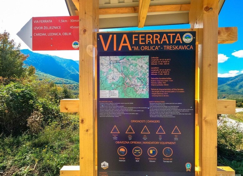 A wooden signpost with information about the 'VIA FERRATA 'M. ORLICA' - TRESKAVICA' mountain route, including distances, technical characteristics, and safety instructions. 1