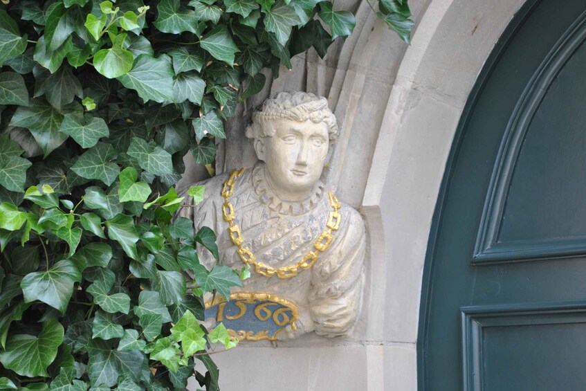 A stone bust with a gold chain, partially covered by green ivy. 5