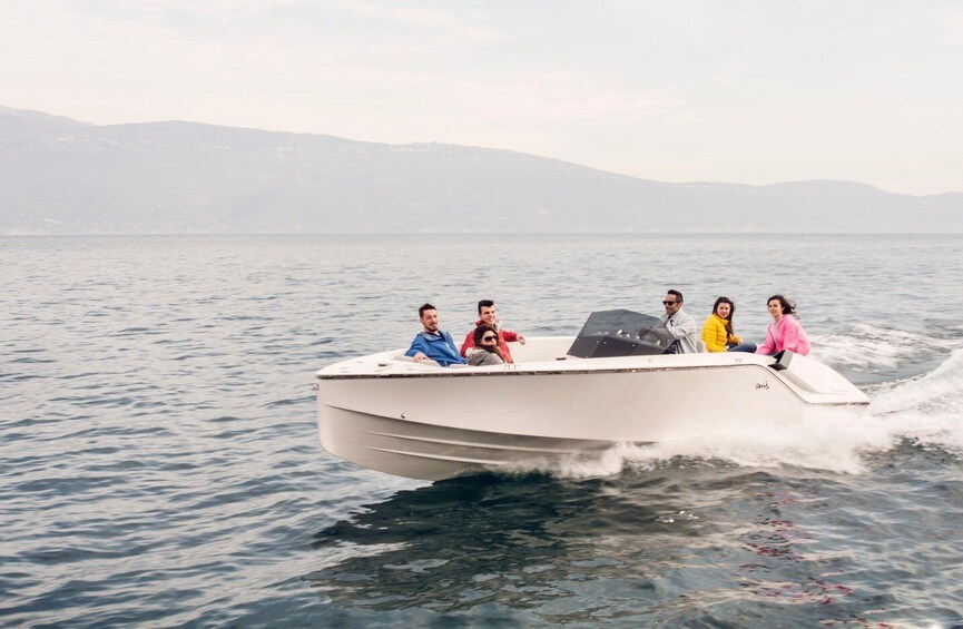 Un bateau à moteur blanc avec cinq personnes à bord, naviguant sur l’eau, avec des montagnes en arrière-plan. 5