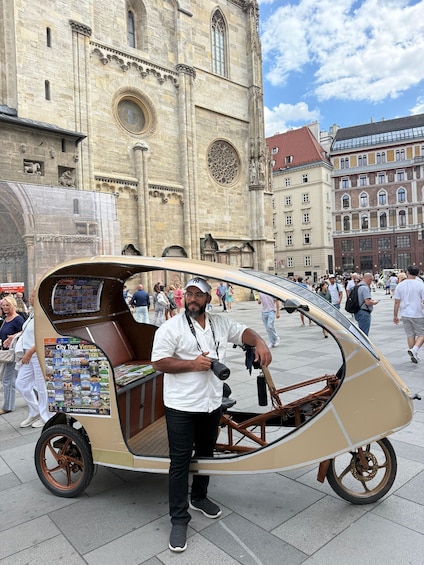 A man in a vintage car-like vehicle with a camera, standing in front of a historic building with a large circular window and intricate stonework. 1