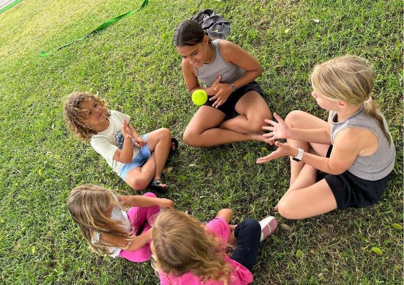 Four children sitting on grass, engaged in a conversation. 3