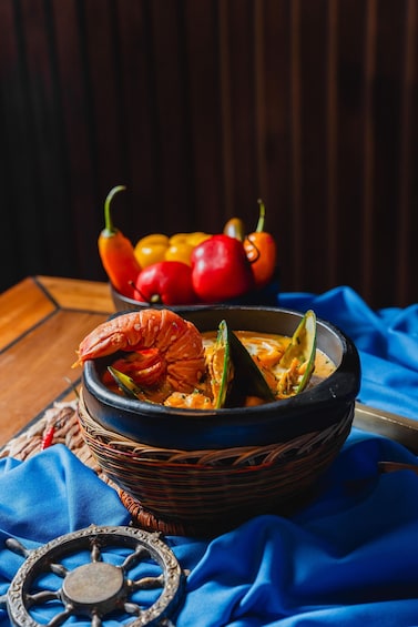 A bowl of seafood stew with a lobster claw, mussels, and a wooden bowl on a blue cloth. 3