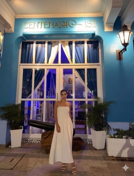 A person in a white dress standing in front of a building with a sign that reads 'CENTENARIO 131'. 4