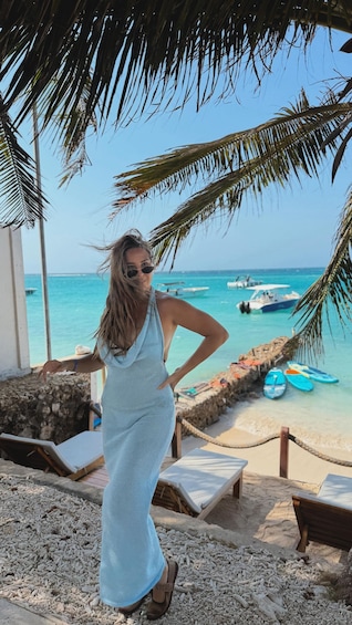 A person standing on a beach with palm trees and boats in the background. 5